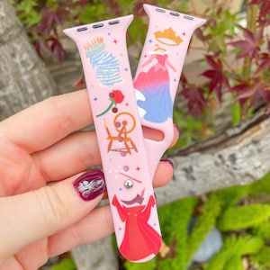 May include: Pink Apple Watch band with a colorful design featuring a princess, a rose, a spinning wheel, and a red dress. The band is made of silicone and has a printed design.