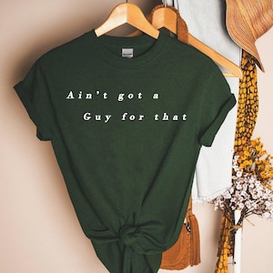 May include: A dark green t-shirt with the text "Ain't got a Guy for that" printed in white on the front.