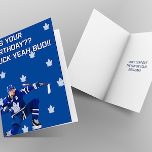 Può includere: Biglietto di compleanno con copertina blu raffigurante un giocatore di hockey con la divisa dei Toronto Maple Leafs. La copertina recita: "IT'S YOUR BIRTHDAY?? PUCK YEAH, BUD!!" All'interno, il biglietto dice: "DON'T LEAF OUT THE FUN ON YOUR BIRTHDAY!!"