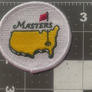 May include: White embroidered patch with the Masters Tournament logo. The logo features a yellow outline of the United States with a red flag and the word "Masters" above it.