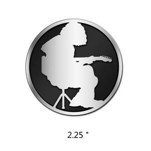 May include: A silver metal pin with a black and white silhouette of a person sitting on a stool and playing a guitar. The pin is 2.25 inches in diameter.