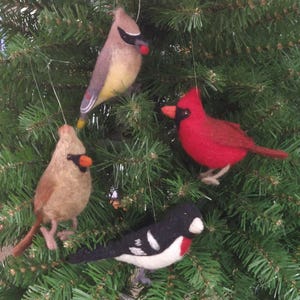 May include: Four felt bird ornaments in various colors, hanging on a Christmas tree. The birds include a red cardinal, a black and white bird, and two tan birds. Each bird has a wire loop for hanging.