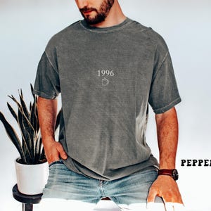 May include: A gray t-shirt with the year "1996" and a small coffee cup graphic printed on the front. The shirt is a relaxed fit and has a slightly faded appearance. The word "PEPPER" is printed in bold, black letters.