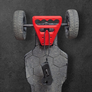 Puede incluir: Un monopatín eléctrico con un asa roja y ruedas negras. La tabla tiene una superficie gris texturizada con un patrón de panal. Un mando a distancia negro cuelga de la tabla.