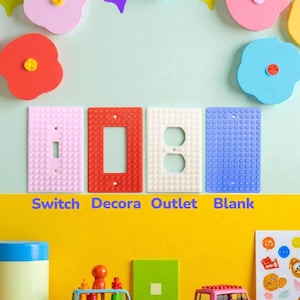 May include: A collection of colorful electrical switch plates and toy cars. The switch plates are pink, red, white, and blue, with the words "Switch Decora Outlet Blank" printed below. The toy cars are blue and pink.