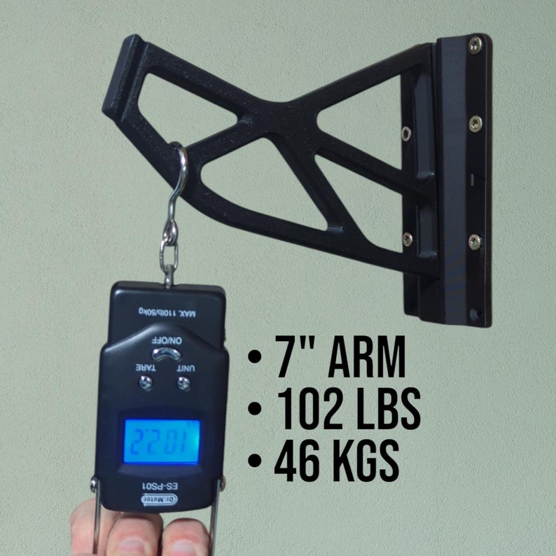 May include: Black metal wall-mounted bracket with a 7-inch arm. A digital scale with a blue display is suspended from the bracket. The text indicates a weight capacity of 102 lbs and 46 kgs.
