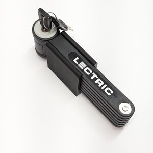 Pu&ograve; includere: Lucchetto pieghevole nero per bicicletta con la scritta "LECTRIC" in bianco. Il lucchetto &egrave; composto da pi&ugrave; segmenti collegati e include una chiave e un cilindro della serratura. Progettato per proteggere biciclette e altri oggetti.