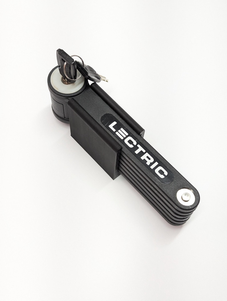 Pu&ograve; includere: Lucchetto pieghevole nero per bicicletta con la scritta "LECTRIC" in bianco. Il lucchetto &egrave; composto da pi&ugrave; segmenti collegati e include una chiave e un cilindro della serratura. Progettato per proteggere biciclette e altri oggetti.