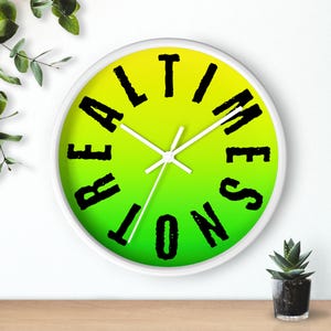 Puede incluir: Reloj de pared con marco blanco y esfera degradada amarillo-verde. La esfera del reloj presenta las palabras "REAL TIME ZONE" en letras negras y estilizadas. Las manecillas del reloj son blancas y el reloj está contra una pared blanca.
