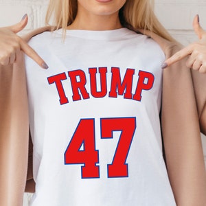 以下が含まれることがあります： 白地に赤と青の文字で「TRUMP 47」と書かれたTシャツです。