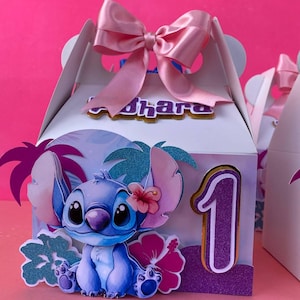 May include: A white favor box with a pink bow, decorated with a blue Stitch character, a pink flower, and green palm trees. The box has a purple number "1" and the name "Ohara" on the front.
