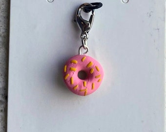 May include: A pink donut charm with yellow sprinkles, attached to a silver metal lobster clasp.