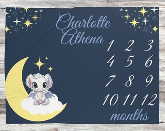 May include: A blue baby milestone blanket with a white dragon on a yellow crescent moon. The blanket has a star pattern and the text "Charlotte Athena 1 2 3 4 5 6 7 8 9 10 11 12 months".