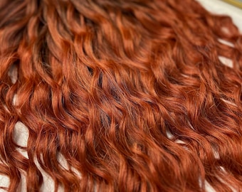 May include: A bundle of wavy, reddish-brown hair extensions. The hair features a gradient effect, shifting from a darker brown at the roots to a bright, fiery red-orange at the ends. The texture appears soft and voluminous.