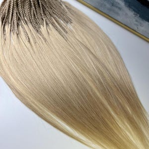 Op de afbeelding: Een set blonde haarverlengingen van echt haar met een lichtbruin ombre-effect. Het haar is gevlochten en klaar om te worden geplaatst.