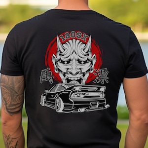 以下が含まれることがあります： 黒いTシャツに、白い日本の悪魔のマスク、赤い円、黒い車、そして「180SX」という文字と「雷」と「魂」という日本語の文字が描かれている。