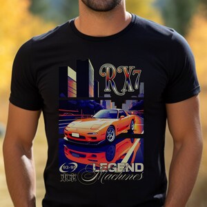 Könnte beinhalten: Ein schwarzes T-Shirt mit einem Grafikdruck eines roten und orangefarbenen RX7 Sportwagens, der auf einer Stadtstraße fährt. Der Text "LEGEND MACHINES" befindet sich unter dem Auto, und der Text "93-95" befindet sich über dem Auto. Das Auto spiegelt sich in der Straße darunter.