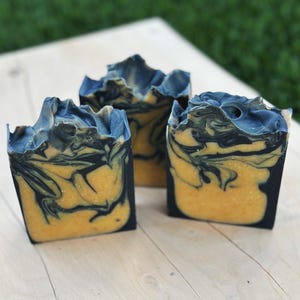 Peut inclure: Trois savons faits à la main avec un motif marbré noir et jaune. Le savon est sur une surface en bois.