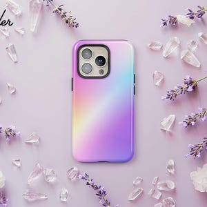 A purple and pink phone case with a gradient design is placed on a pink background, surrounded by scattered crystals and lavender flowers.