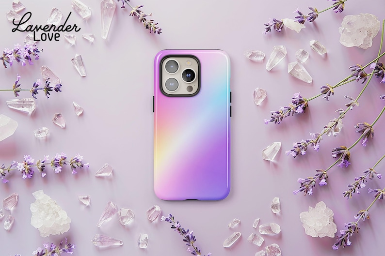 A purple and pink phone case with a gradient design is placed on a pink background, surrounded by scattered crystals and lavender flowers.