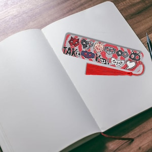 May include: A red and white bookmark with a red tassel. The bookmark has a pixelated design with various symbols and the text "Take Your Time".
