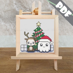 May include: Cross stitch pattern featuring a cute ghost wearing a Santa hat, a reindeer with a skull, and a Christmas tree with candy canes. The pattern is displayed on a wooden easel.