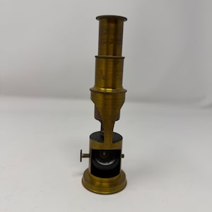 May include: A vintage brass microscope with a cylindrical body and adjustable focus knob. The microscope has a flared base and a series of stacked cylindrical sections, typical of antique scientific instruments. The brass has a warm, aged patina.