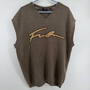 以下が含まれることがあります： 前面に金色の筆記体で「Fubu」の文字が入った茶色のVネックセーターベスト。袖なしのベストで、裾はリブ編みです。「Fubu Sports」のブランド名がネックラベルに表示されています。