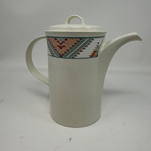 May include: Cream-colored ceramic coffee pot with a lid and a handle. The pot features a decorative band with a geometric pattern in shades of brown, green, and white. The spout is long and curved.