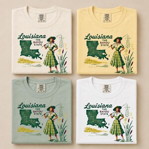 May include: Four t-shirts in cream, yellow, sage green, and white, each featuring a graphic design. The design includes the word "Louisiana", the phrase "The Bayou State", and an illustration of a woman, a map, and a power line.