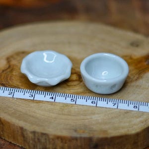 以下が含まれることがあります： 2つの小さな水色の陶器のボウル。1つはスカラップエッジの丸型、もう1つはシンプルな丸いボウルです。ボウルの横に定規が置かれています。ボウルは木製の表面にあります。