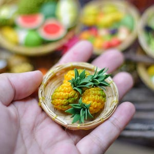 Può includere: Un piccolo cestino intrecciato contiene tre ananas in miniatura con cime verdi e corpi gialli. Gli ananas sono disposti in un piccolo cestino intrecciato.