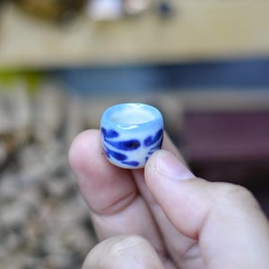 Könnte beinhalten: Ein kleiner Keramikring mit blau-weißem Muster. Der Ring wird in einer Hand gehalten und hat eine hellblaue Innenseite und dunkelblaue Pinselstriche auf der Außenseite. Der Ring hat einen Durchmesser von etwa 2,5 cm.