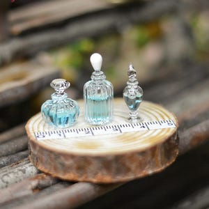 Puede incluir: Tres botellas de vidrio en miniatura con líquido azul sobre una rodaja de madera. Las botellas tienen diferentes formas y tapones. La rodaja de madera tiene una regla impresa.