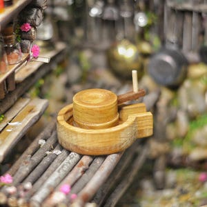 May include: A miniature wooden grain mill with a crank handle, set on a rustic wooden surface with a background of miniature trees and other details.