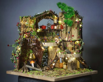 May include: A miniature fairy kitchen scene with a rustic, whimsical design. The scene features a wooden structure with a waterfall, a small stove, and various kitchen items. The scene is decorated with fairy lights and colorful flowers.