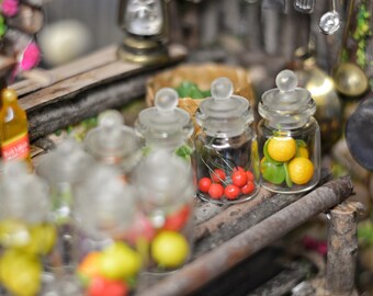 Può includere: Piccoli barattoli di vetro con coperchi trasparenti, riempiti con ciliegie rosse, limoni gialli e lime verdi. I barattoli sono su una superficie di legno rustico, che suggerisce una cucina o una dispensa. Altri oggetti da cucina in miniatura.