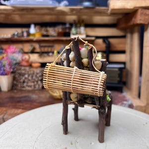 Könnte beinhalten: Miniatur-Rustikstuhl aus Zweigen und kleinen Steinen, mit einer daran befestigten, gerollten Bambusmatte. Der Stuhl ist braun und beige, und die Matte wird von einer beigen Schnur gehalten. Der Stuhl steht auf einer weißen Oberfläche.