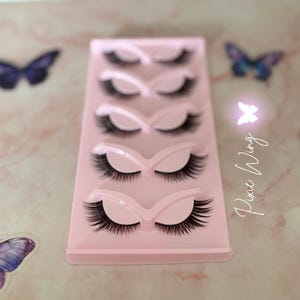 Peut inclure: Un présentoir rose contenant cinq paires de faux cils noirs. Le présentoir est orné d'autocollants papillon et du texte "Pixie Wing".