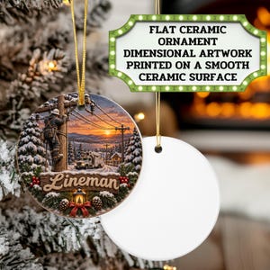 May include: A round ceramic ornament featuring a printed scene of a lineman working on a utility pole at sunset, with snow-covered pine trees and a utility truck. The word Lineman is written in script. A second blank white ornament is also shown.