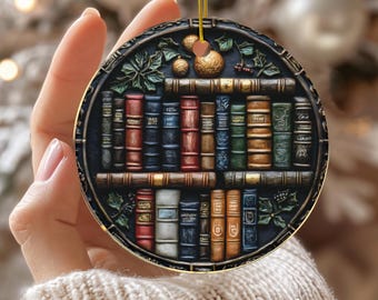 Puede incluir: Adorno navideño redondo de cerámica con un diseño detallado de estantería con varios libros coloridos. El adorno tiene un borde dorado y una cuerda dorada para colgar. La palabra "CERAMIC" está impresa en la parte inferior.