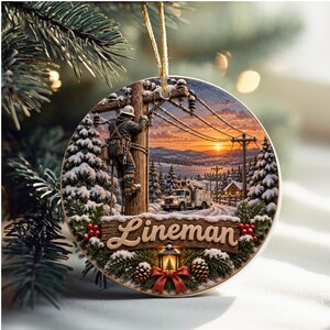 May include: A round Christmas ornament featuring a graphic of a utility worker climbing a wooden pole at sunset. The scene includes snow-covered pine trees, a utility truck, and a lantern. The word Lineman is printed in a script font.