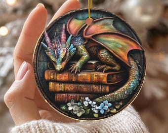 May include: Round ceramic ornament featuring a colorful dragon resting on a stack of books. The dragon has rainbow-colored horns and wings. The ornament has a gold string for hanging and the word "CERAMIC" is printed at the bottom.