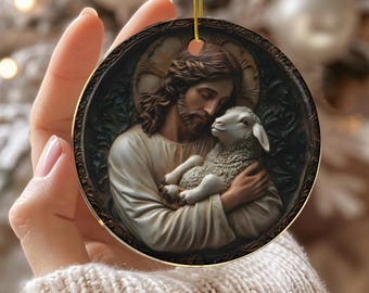 Può includere: Ornamento natalizio rotondo in ceramica con un rilievo dettagliato di Gesù che tiene un agnello. L'ornamento ha un bordo dorato e un cordino dorato per appenderlo. La parola "CERAMIC" è stampata in basso.