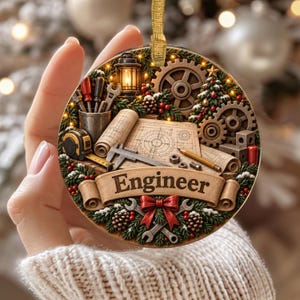Könnte beinhalten: Ein runder Weihnachtsschmuck mit einem Banner mit der Aufschrift Engineer, umgeben von Ingenieurwerkzeugen wie einem Messschieber, einem Maßband, Bauplänen, Zahnrädern, einer Laterne und Tannenzweigen mit einer roten Schleife und Tannenzapfen.