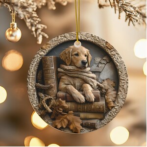 May include: A round Christmas ornament featuring a golden retriever puppy nestled among books and wearing a scarf. The ornament has a detailed, embossed border and is suspended by a gold cord. Autumn leaves are also present.