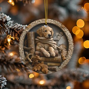 May include: A round, decorative ornament featuring a golden retriever puppy wearing a scarf and resting on a stack of books. The ornament has a detailed, embossed border and is suspended by a gold cord. Autumn leaves are also featured.