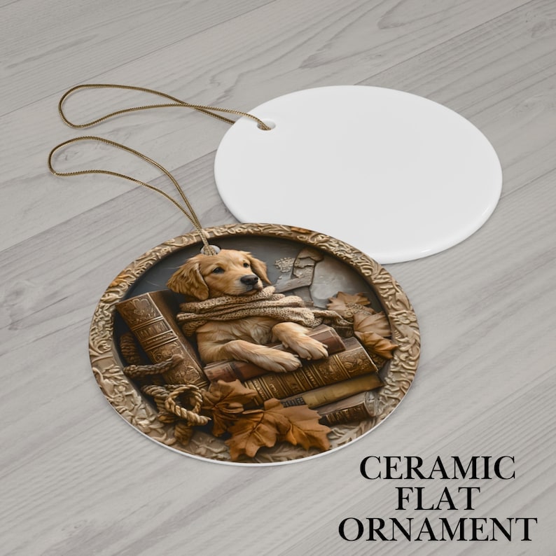 May include: A ceramic flat ornament featuring a golden retriever puppy lying on books, wearing a scarf. The ornament has a detailed, embossed design with a rope and autumn leaves. A blank white ceramic disc is next to it.