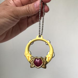 May include: A yellow plastic tambourine keychain with a red heart-shaped gem in the center. The tambourine has a silver chain attached to it.