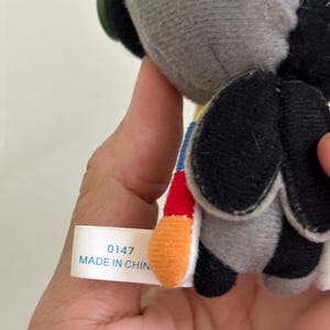 May include: A plush toy with a gray head and black wings. The toy has a colorful tail with red, yellow, and blue accents. A tag reads "0147 MADE IN CHIN".